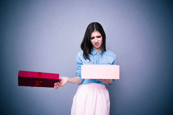 Dissatisfied woman opening gift over gray background