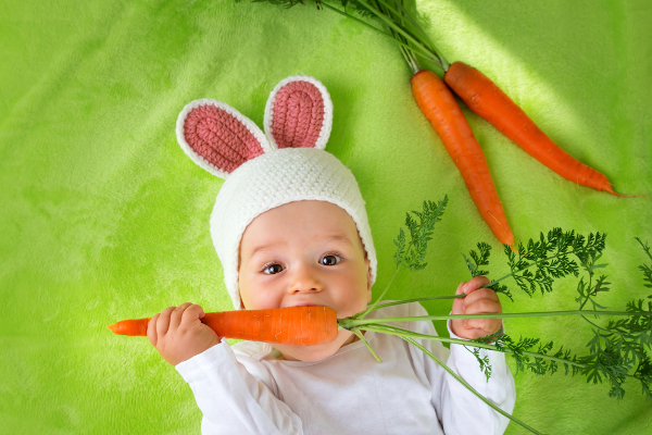 Baby in rabbit hat eating fresh carrot